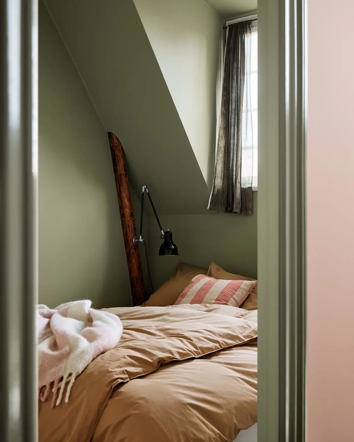 Bedroom with brown bedding and a pink-striped pillow against green painted walls and trims in the Jotun colour 8493 Green Tea.
