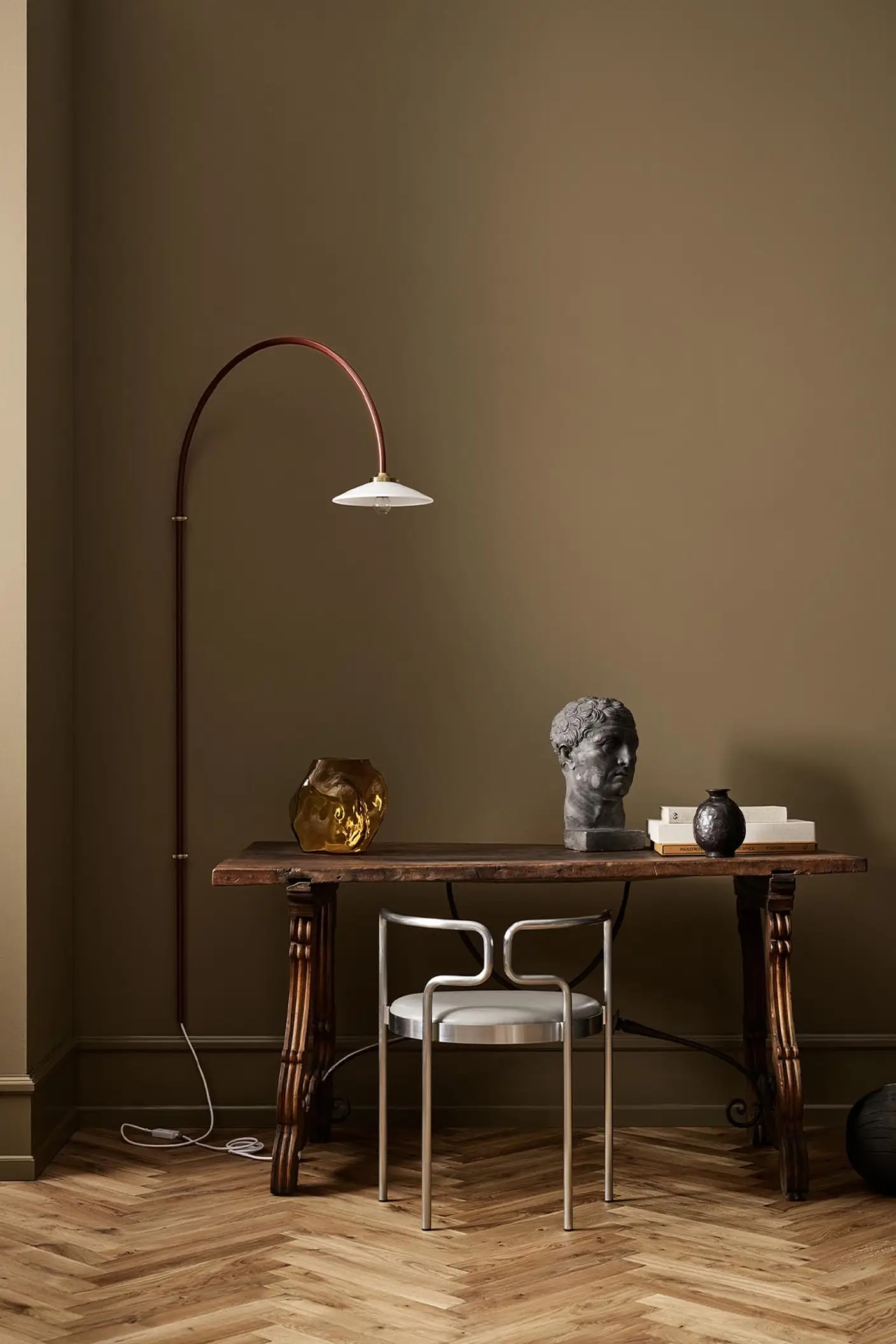 A wooden table, decor, and arched lamp against a golden brown wall in the colour 1974 Golden Walnut from Jotun.